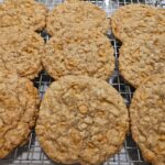 Close-up of freshly baked sourdough discard butterscotch oatmeal cookies with coconut, featuring a golden-brown, soft texture, and visible butterscotch chips, oats, and coconut flakes on a cooling rack.