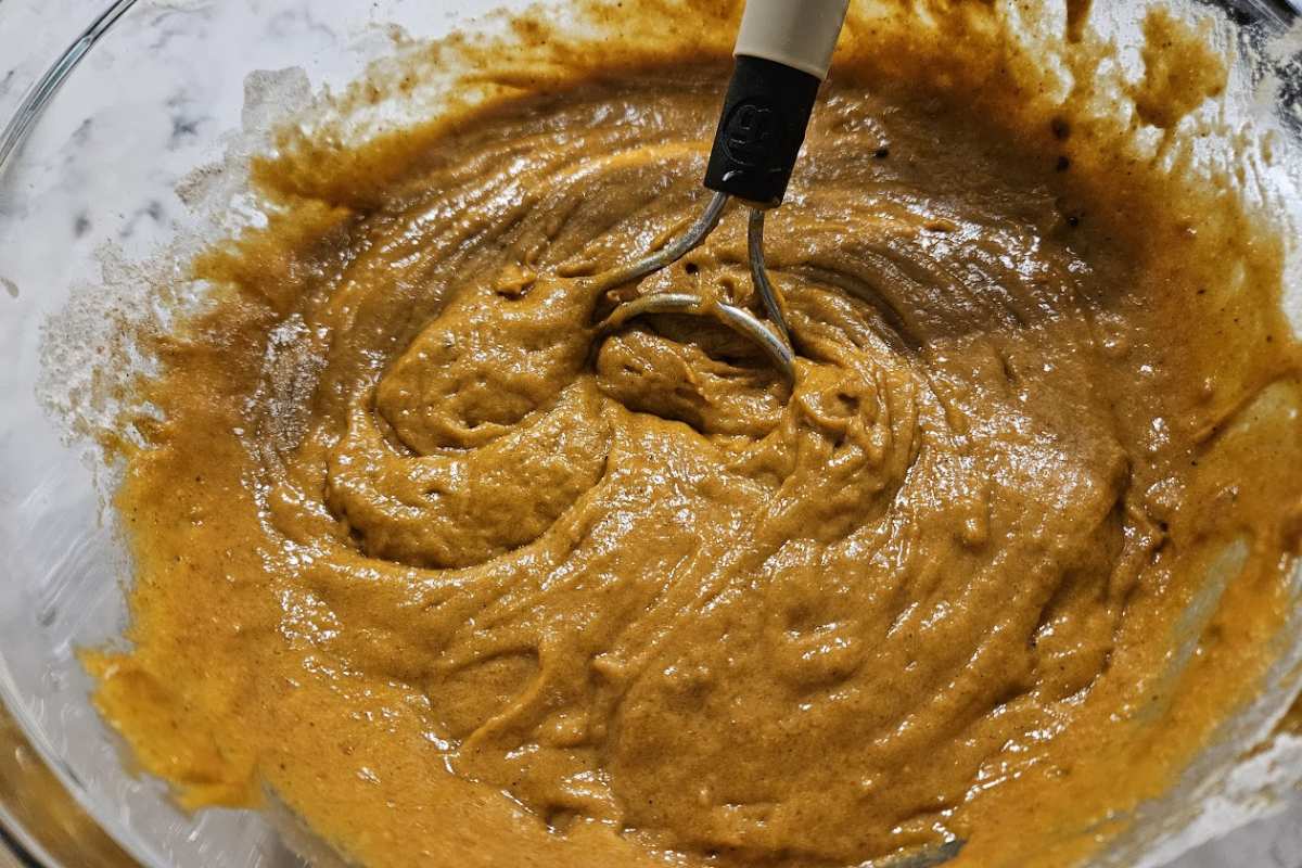 Mixing pumpkin batter for Pumpkin Caramel Pecan Tres Leches Cake in a large bowl, combining the rich fall flavors of pumpkin, cinnamon, and sourdough discard.