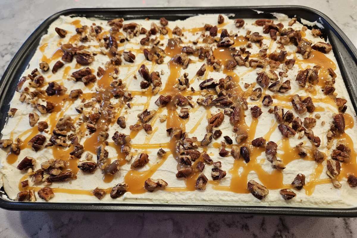 The finished Pumpkin Caramel Pecan Tres Leches Cake in a 9x13 pan, topped with whipped cream, chopped pecans, and a caramel drizzle, ready to serve.